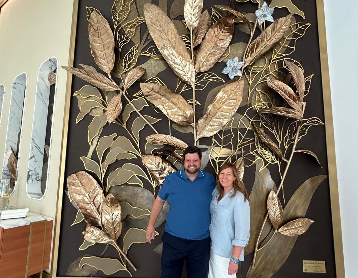 Manu Soriano and his wife posing in an embrace in front of a large decorative golden-leaf mural at ZEM Clinic