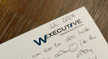 Handwritten letter on W Executive letterhead dated July 2024, resting on a wooden table