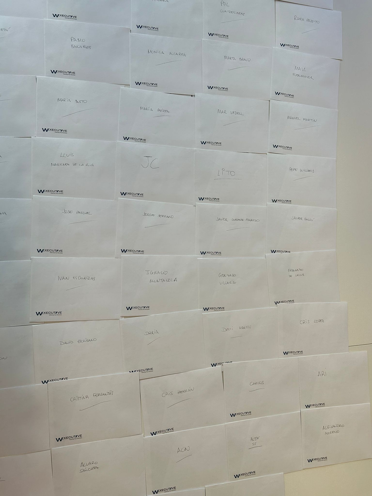 Wall covered in envelopes on W Executive letterhead, each with a team member's name handwritten on it