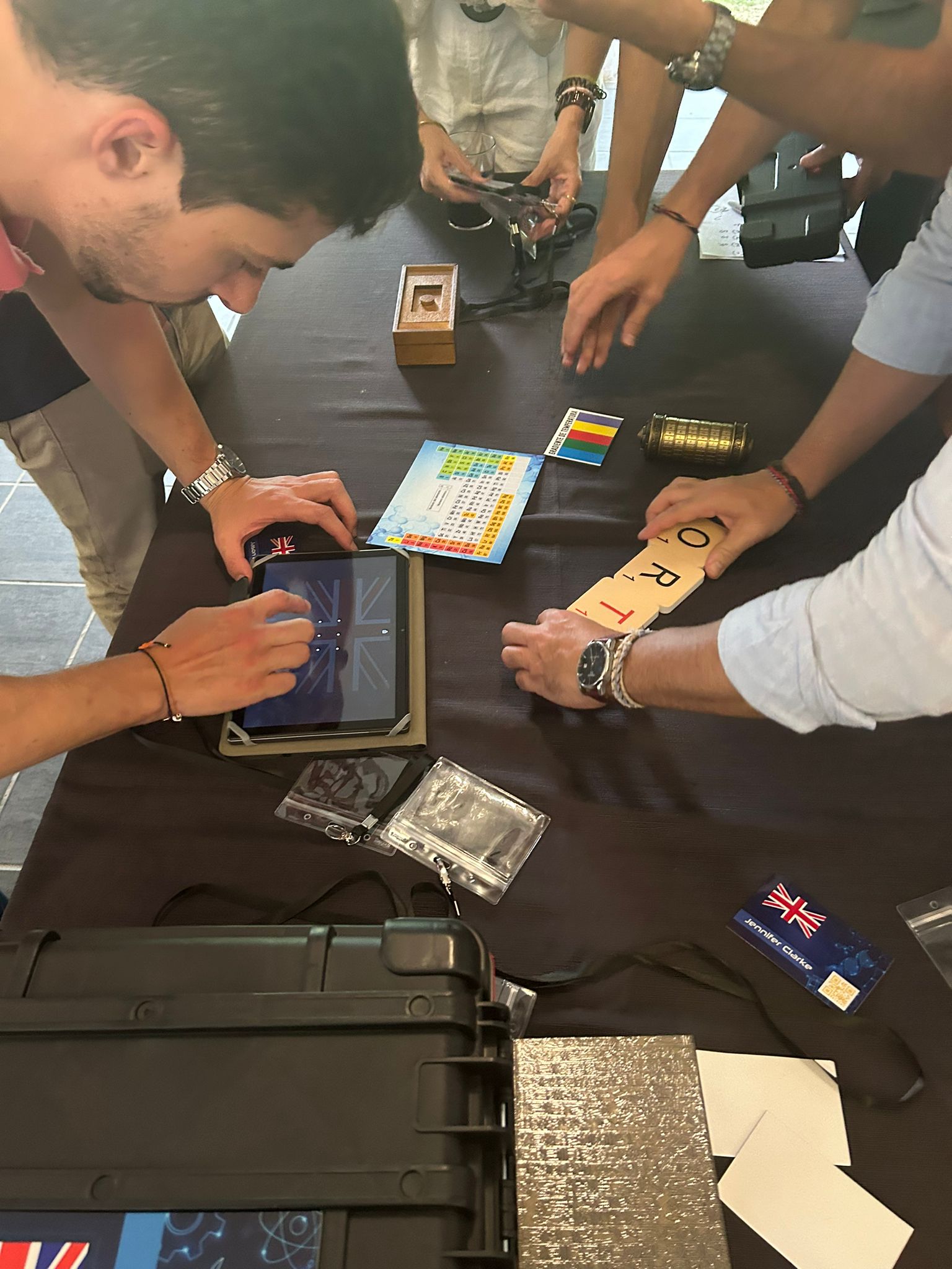 Team solving a riddle with a tablet, tokens and padlocks on a table during the escape room