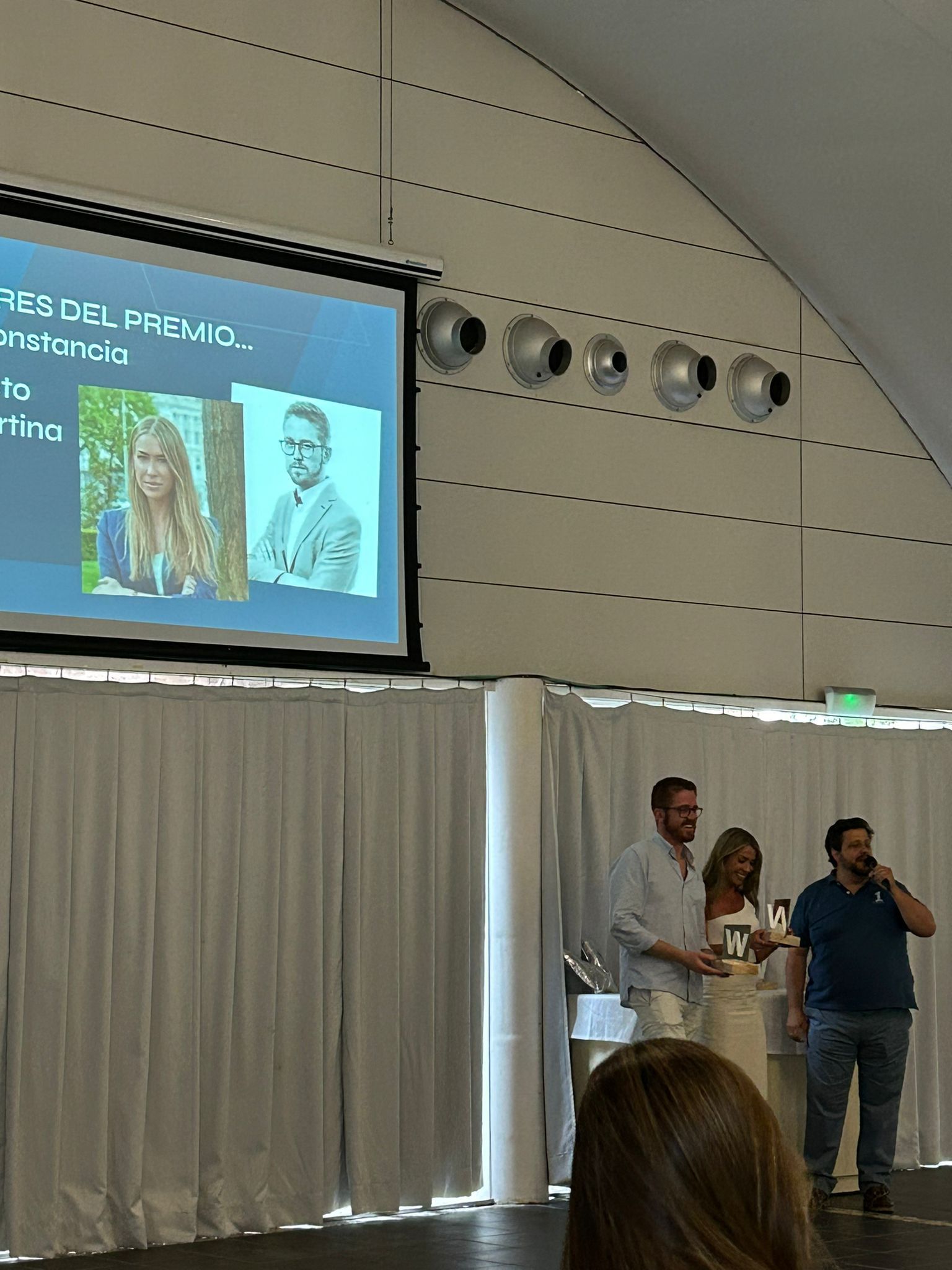 Manu Soriano handing out a W Award on stage while the screen shows the winners