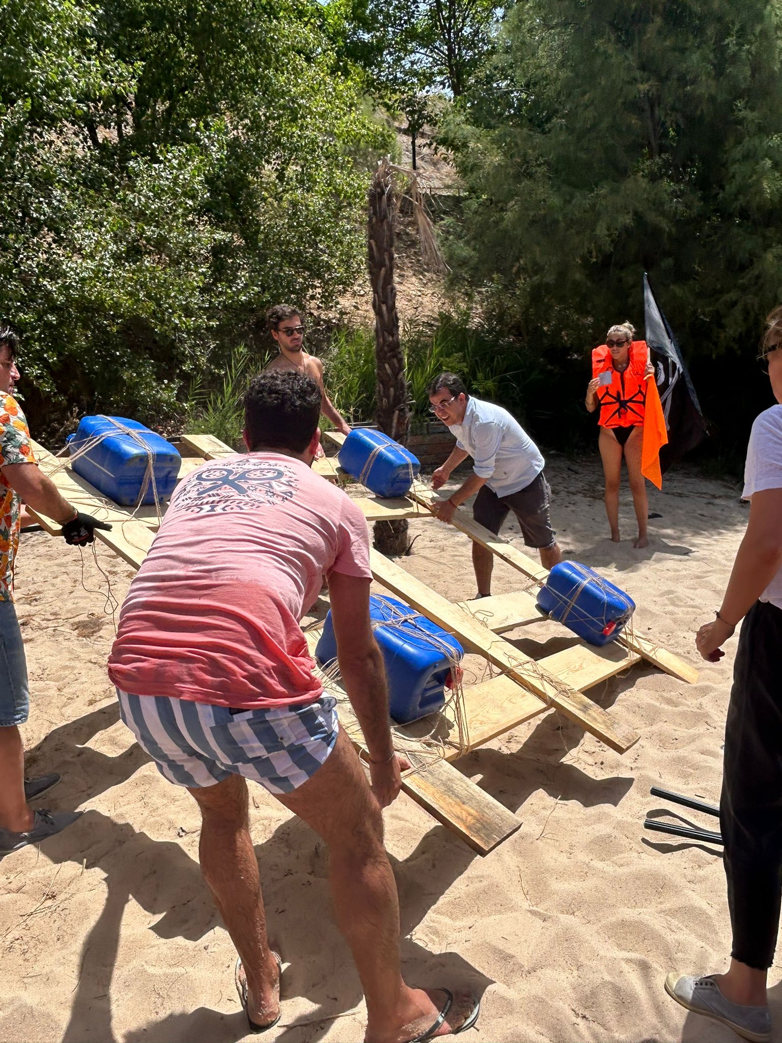 Team members building a raft with planks and barrels on the beach for the team challenge