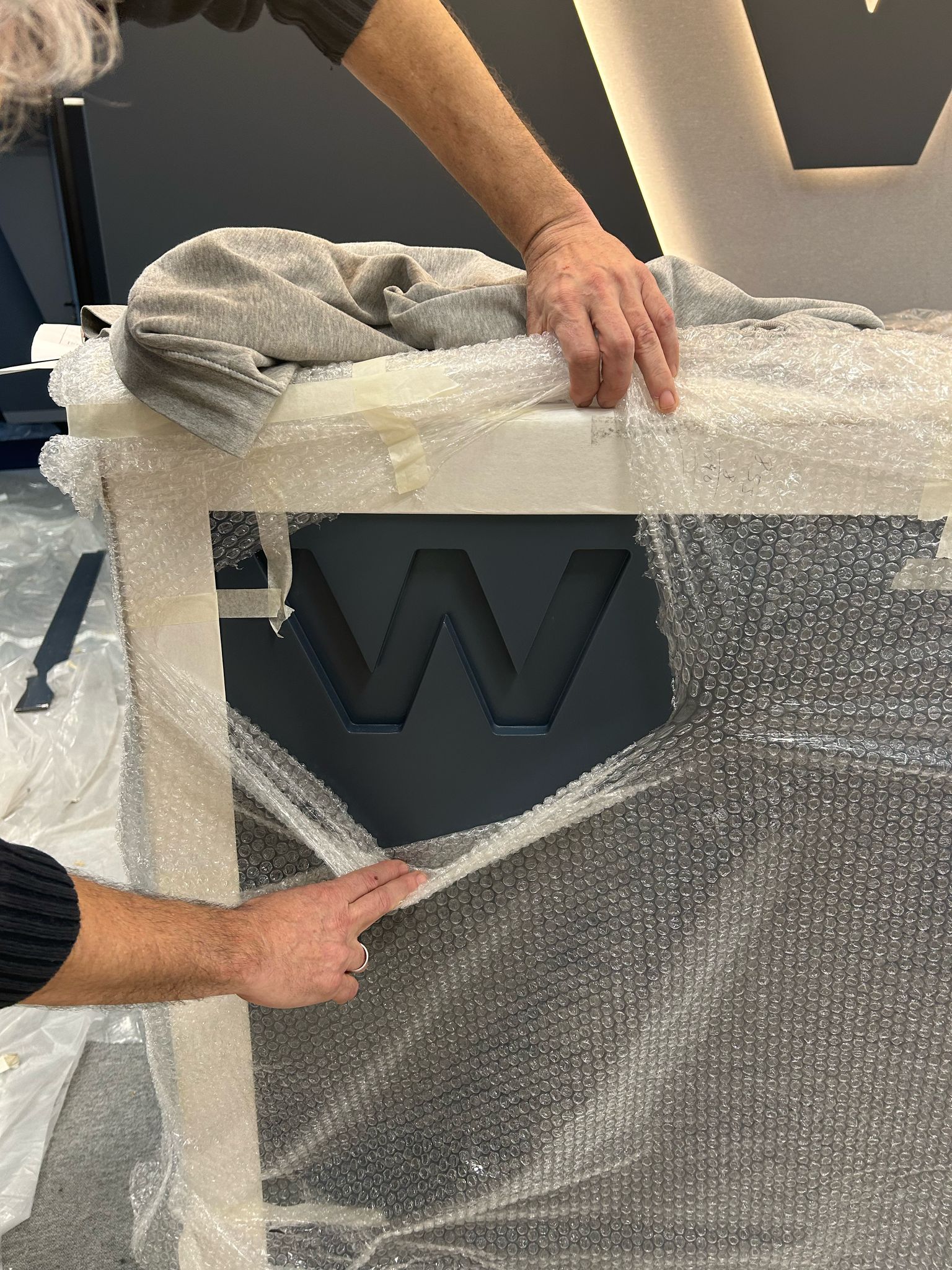 Hands unboxing a reception desk bearing the W logo at the new W Executive headquarters