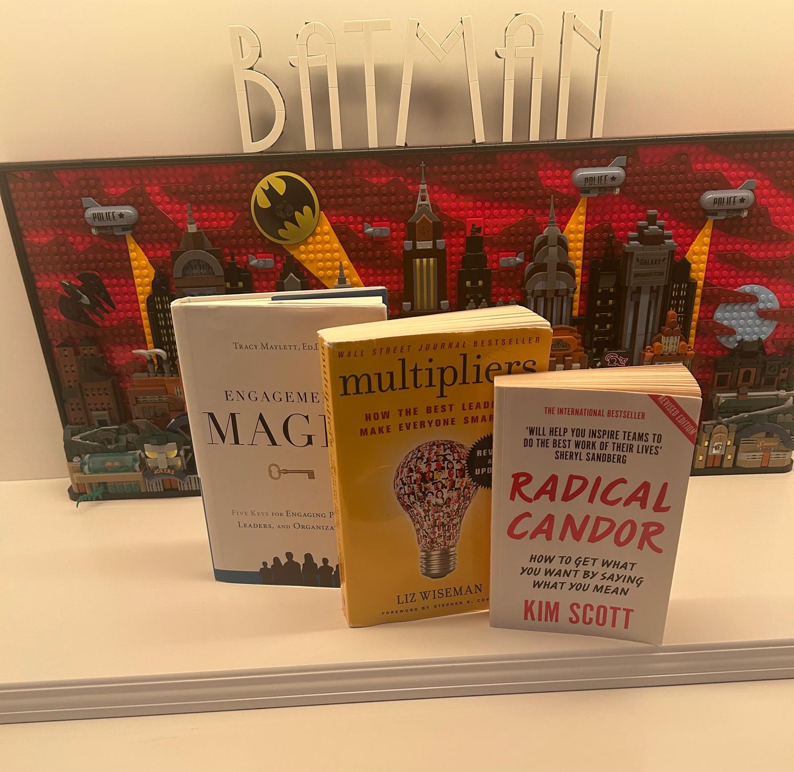 The books Engagement Magic, Multipliers and Radical Candor in front of a Batman painting