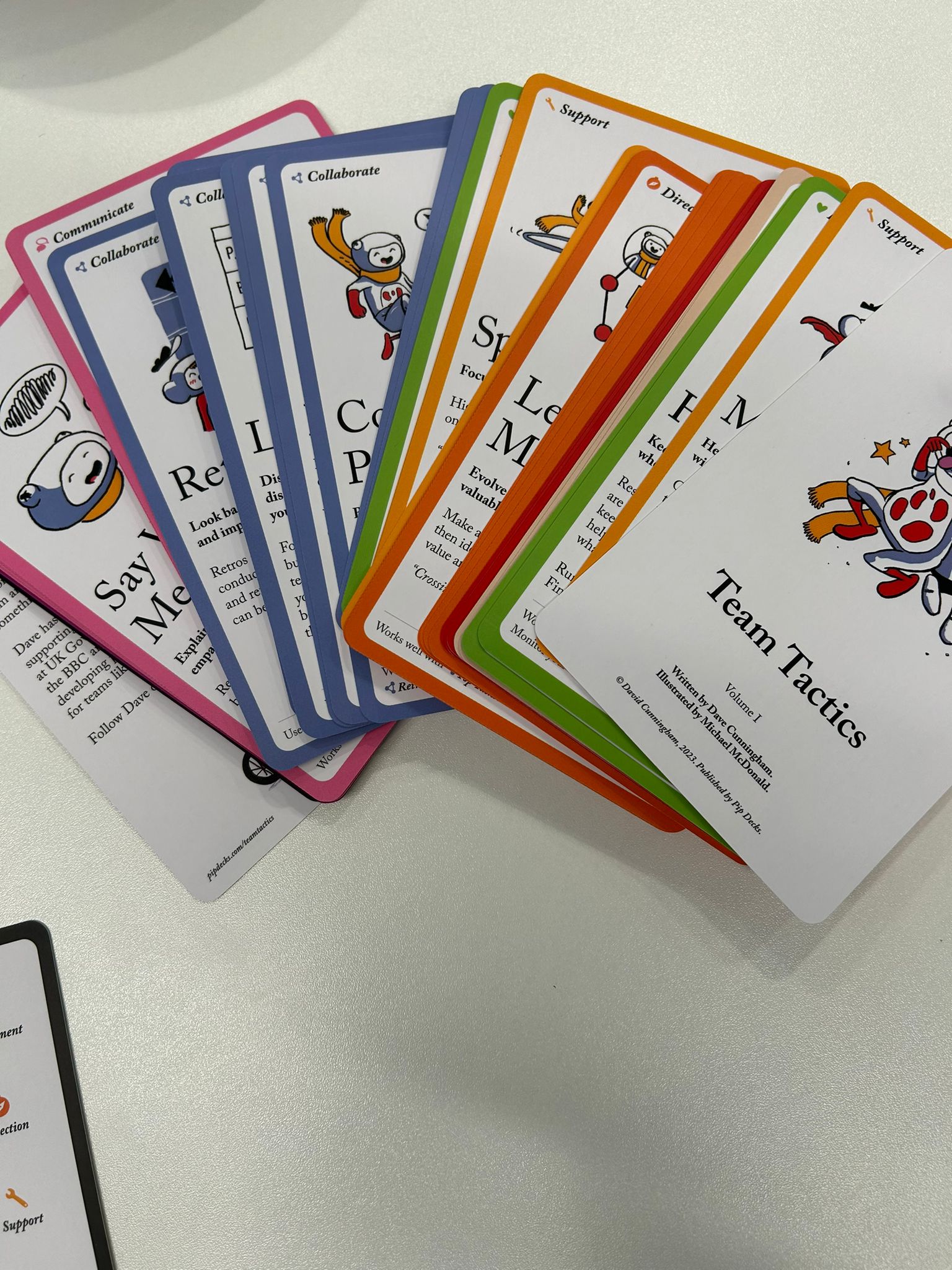 Colorful Team Tactics cards fanned out on a white table