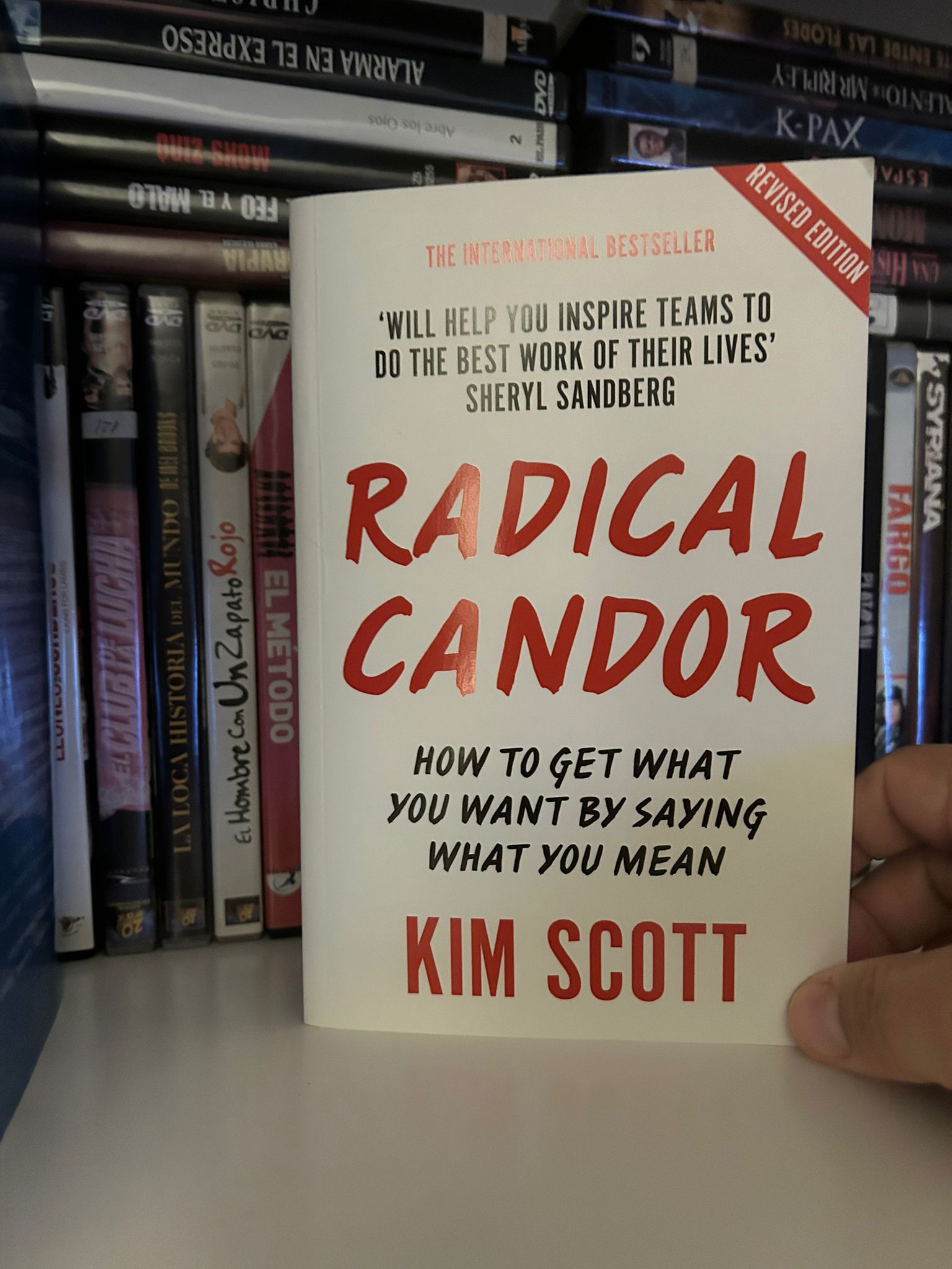 A copy of Kim Scott's book Radical Candor held in front of a shelf of DVDs
