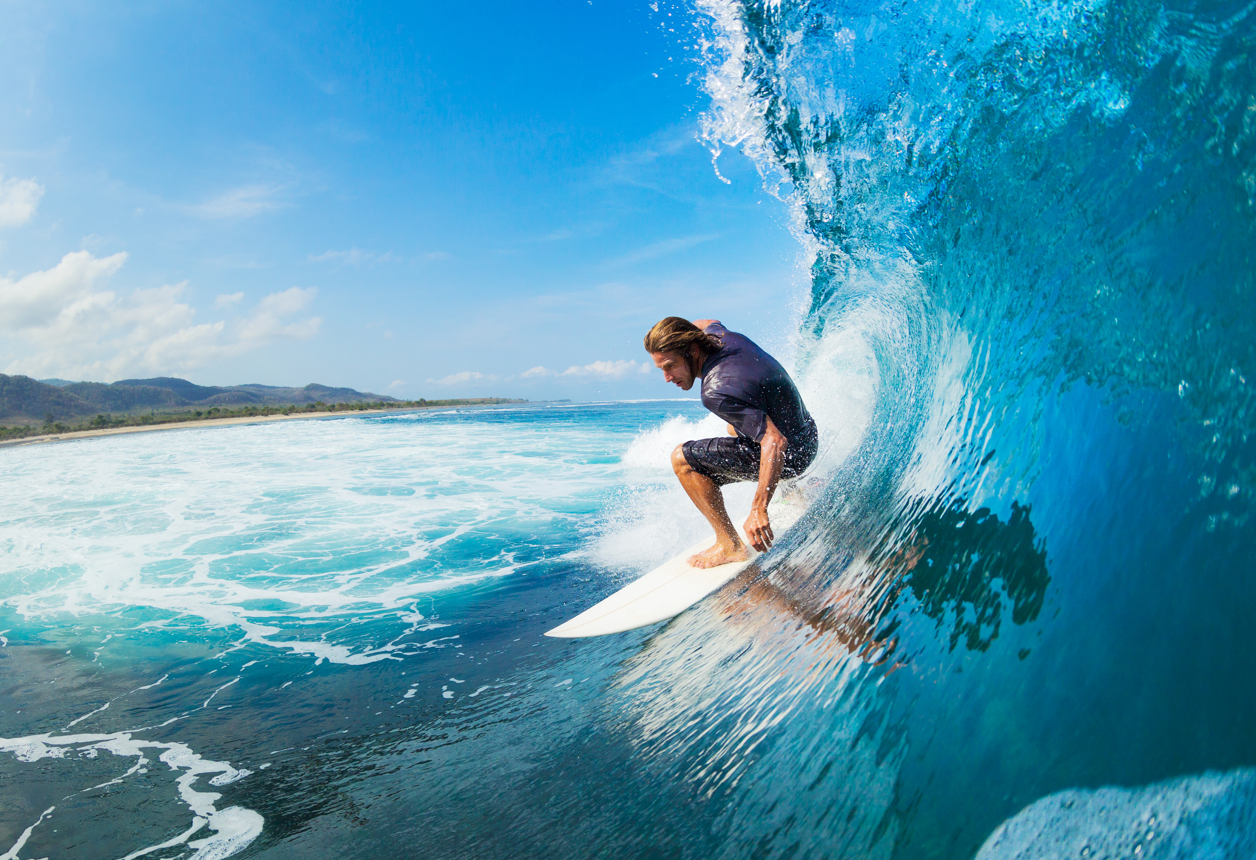 Surfer riding the barrel of a big blue wave near the coast