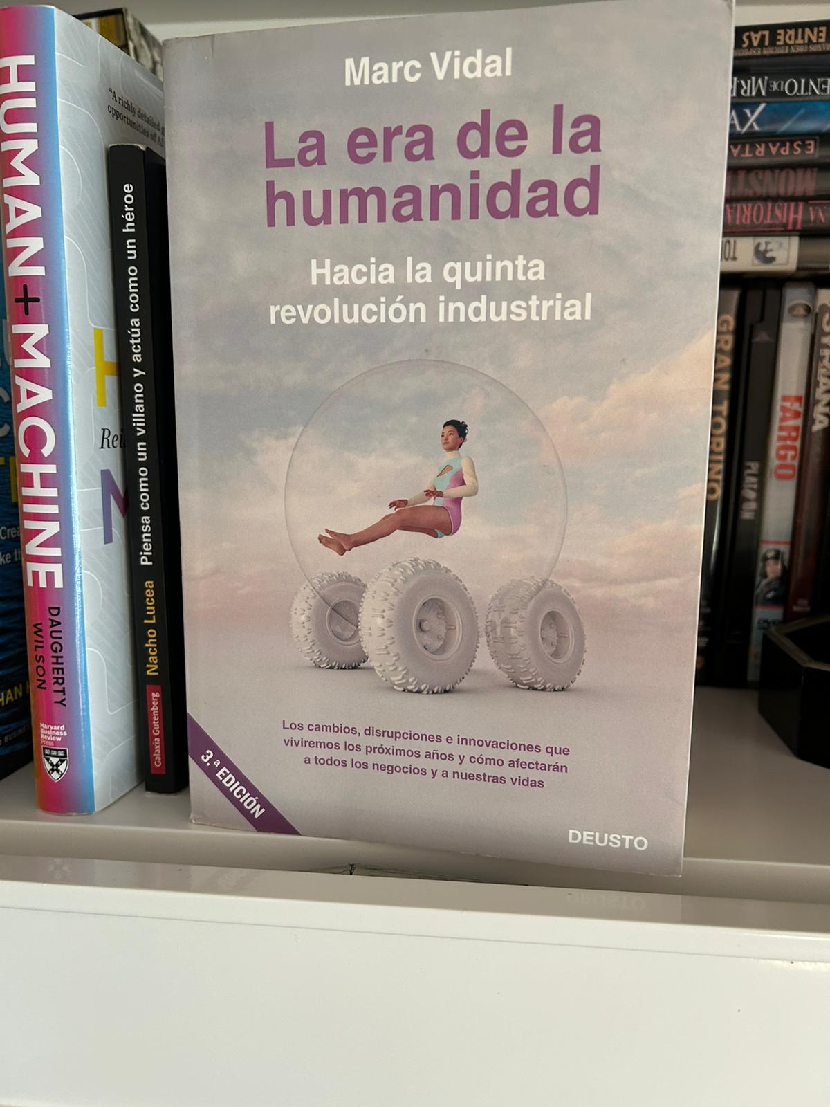 The book The Age of Humanity by Marc Vidal next to Human + Machine on a bookshelf