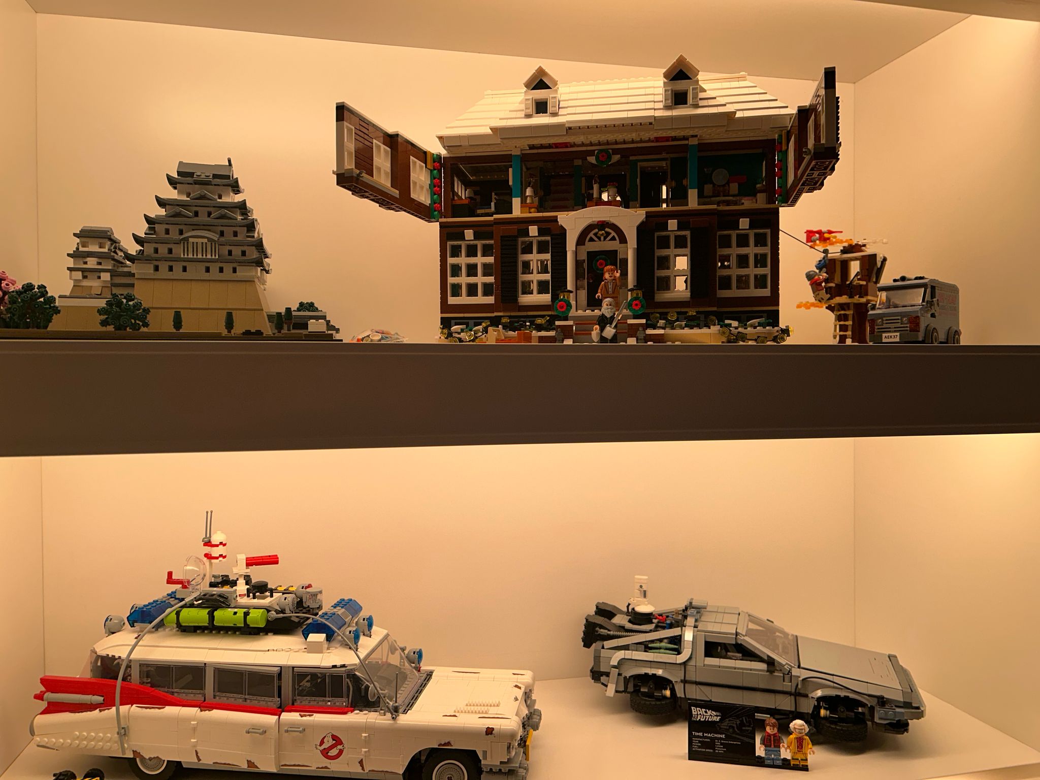 Lit display case with the LEGO collection: a Japanese castle, the Home Alone house, the Ecto-1 and the DeLorean