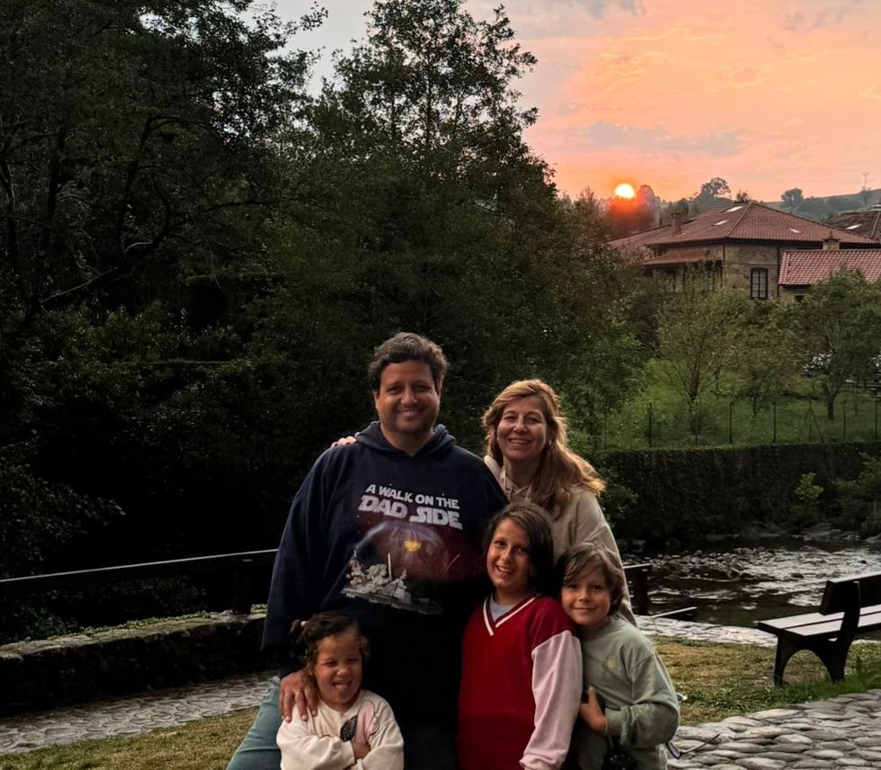 A family of five posing by a river at sunset in a green rural setting
