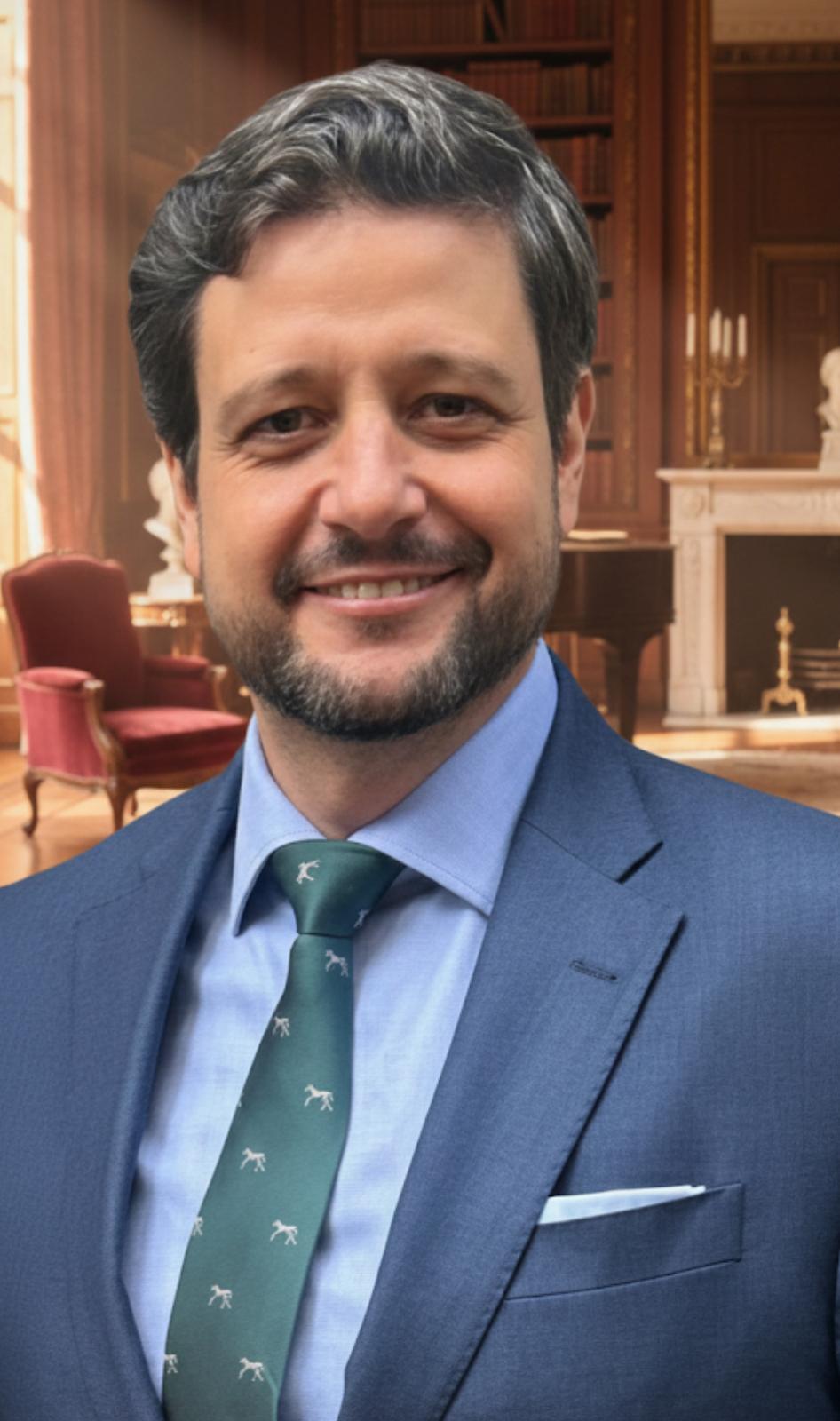 Portrait of Manu Soriano in a blue suit and green tie in a classic library