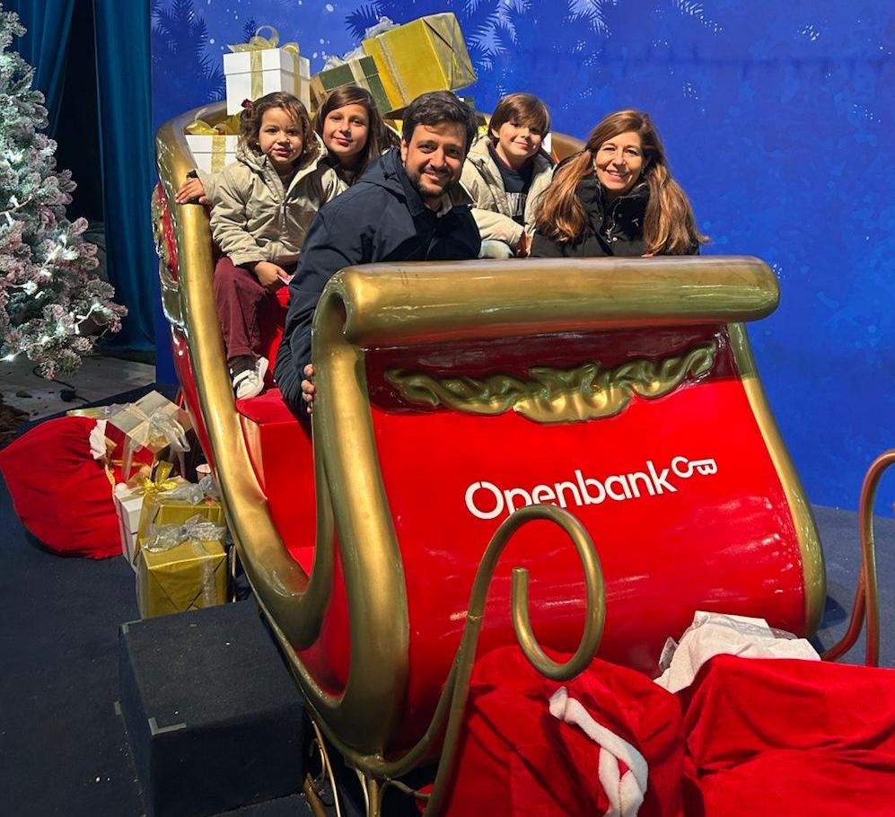 A family of five posing on a red Openbank Christmas sleigh surrounded by gifts