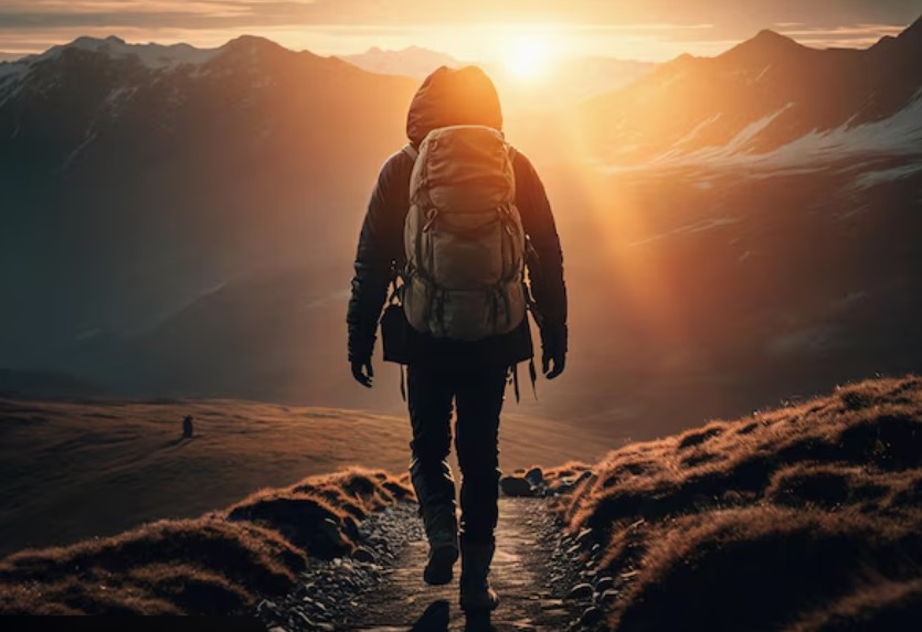 Hiker seen from behind with a backpack walking toward the rising sun between mountains